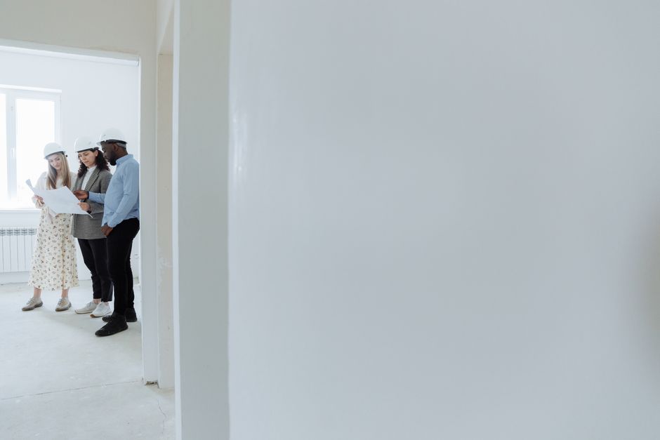Architects wearing hard hats review blueprints inside a building under construction.