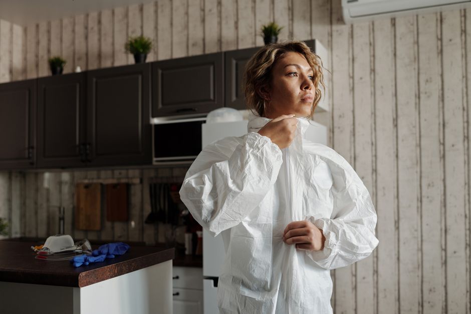 Woman in personal protective equipment zipping up suit in a kitchen setting.