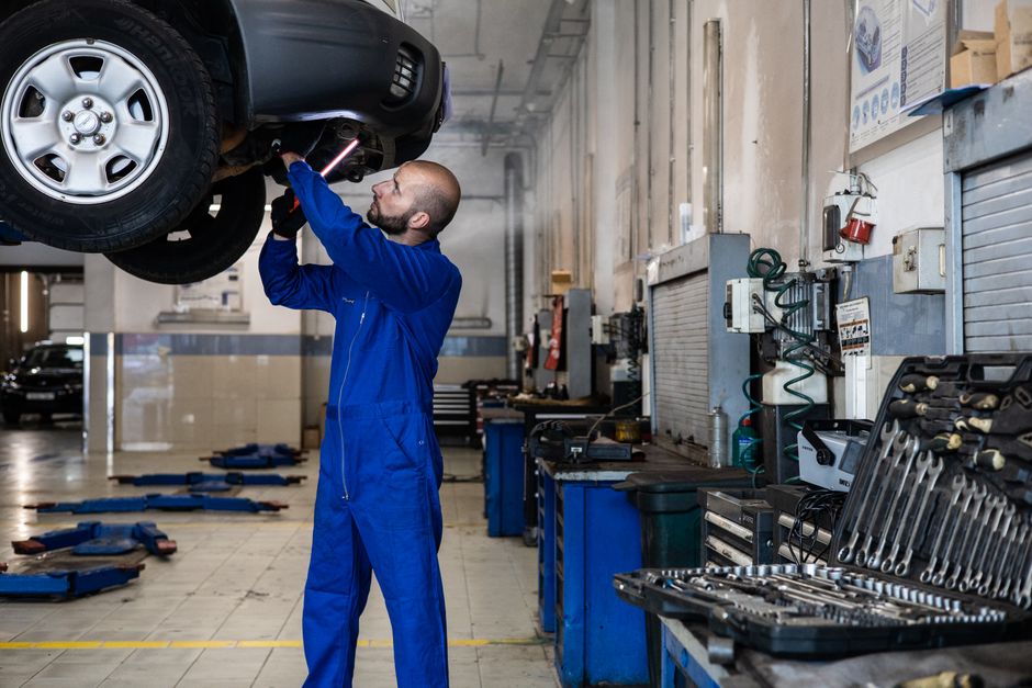 Mechanic inspecting a raised car in an auto workshop for maintenance and repair services.
