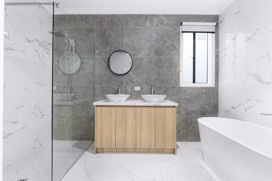 A sleek and stylish modern bathroom with minimalist design, featuring dual washbasins, marble tiles, and a glass shower enclosure.