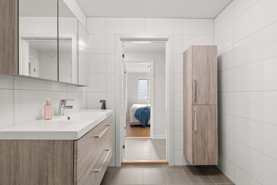 A sleek, modern bathroom showcasing minimalist wooden cabinetry and white tiles.