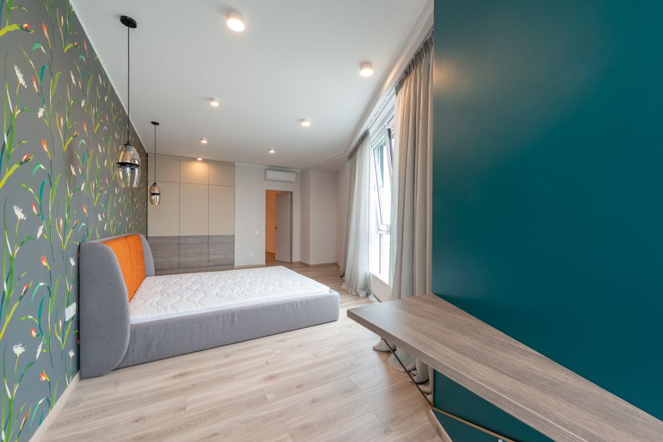 Bed with mattress between decorative lamps hanging on ceiling against wall with floral ornament in house