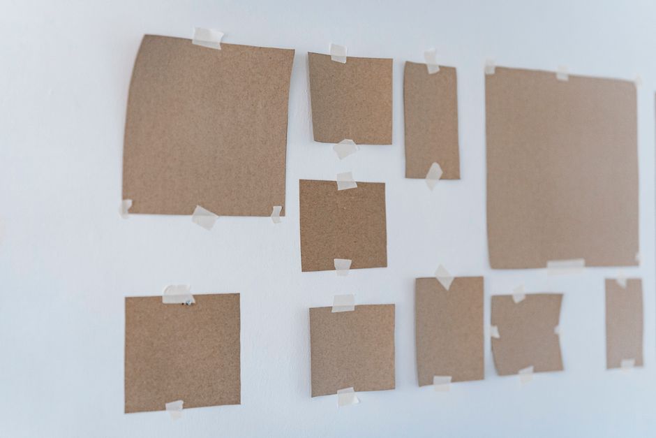 A minimalist arrangement of cardboard pieces taped to a white wall, creating an artistic abstract display.