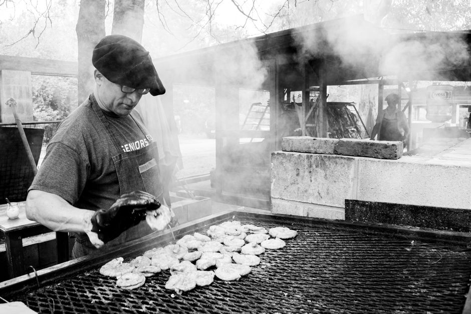 Grillmaster cooking chicken patties at outdoor barbecue, smoky atmosphere.