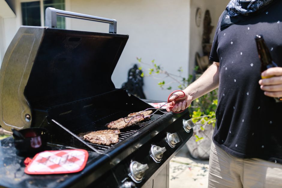 Person grilling steaks on barbecue outdoors, enjoying a sunny day.