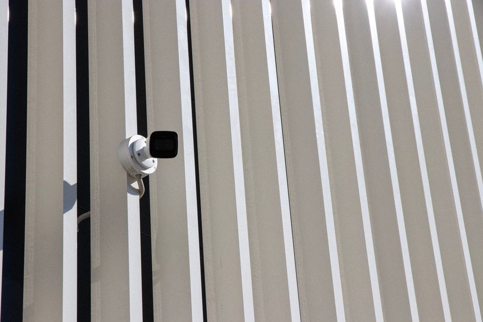 A security camera is mounted on a building with sleek, vertical lines creating a minimalist architectural effect.