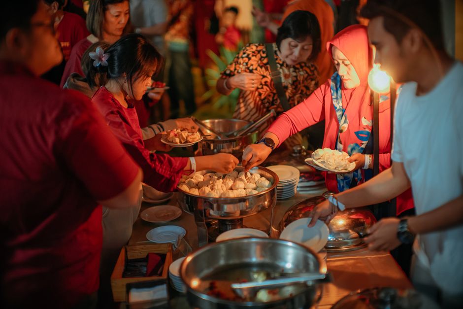 A group of adults engaging in a lively buffet dinner event. Warm lighting and diverse participation.