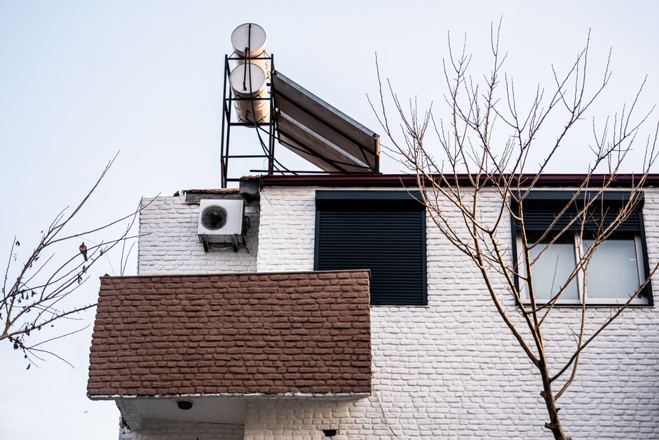 A minimalist building facade with air conditioner and bare winter trees, viewed from a low angle.
