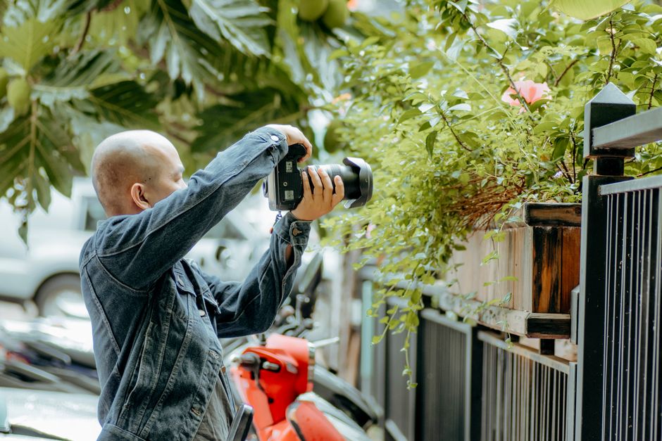 Photographer in denim captures nature amidst urban environment.