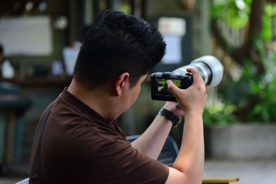 Man focusing camera lens in an outdoor setting, showcasing photography in action.