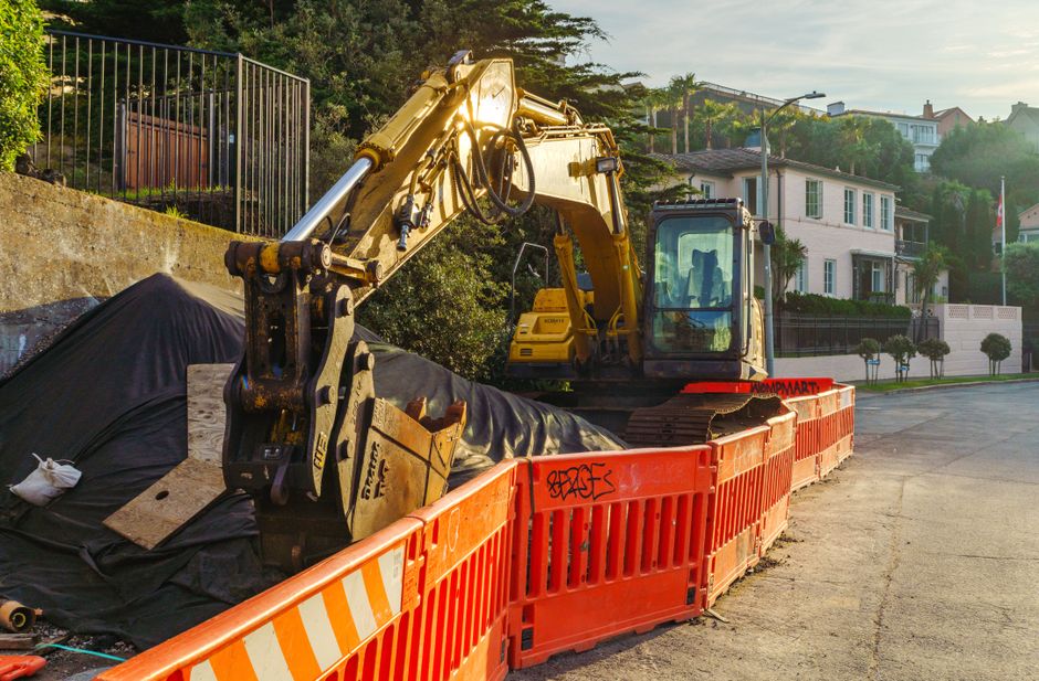 Excavator at a construction site with orange barricades in a residential area.