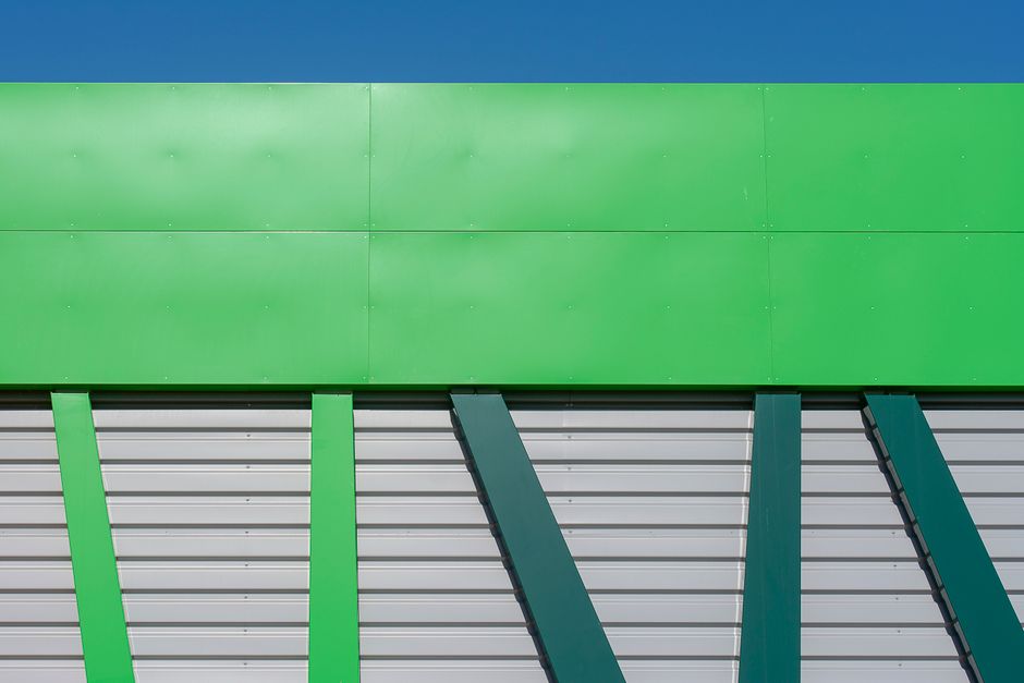 Close-up of a modern green industrial building facade with geometric design against a clear blue sky.