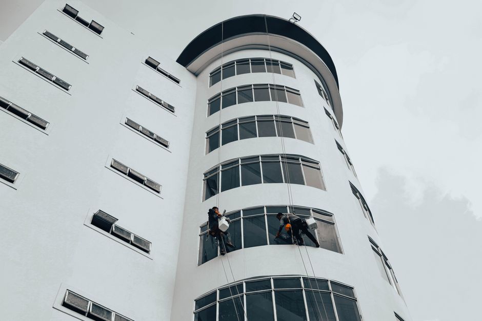 Workers cleaning windows on a modern high-rise building using ropes. Urban architectural maintenance.