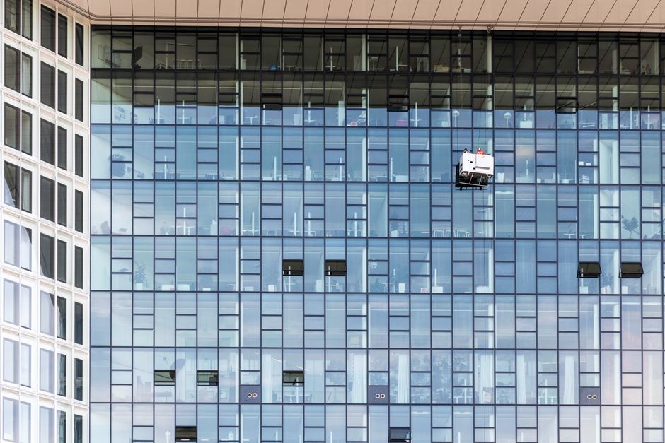 High-rise glass building exterior with window cleaners in Hamburg, Germany.