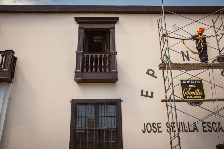 A construction worker paints a building facade while standing on scaffolding, showcasing architectural restoration.