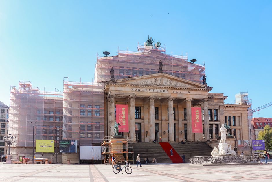 Front view of Konzerthaus Berlin with scaffolding and statue in bright daylight.