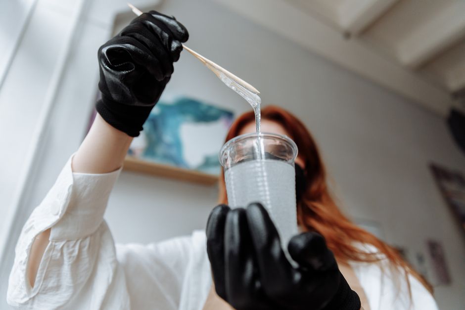 A person demonstrating resin mixing while wearing black gloves indoors with ambient light.