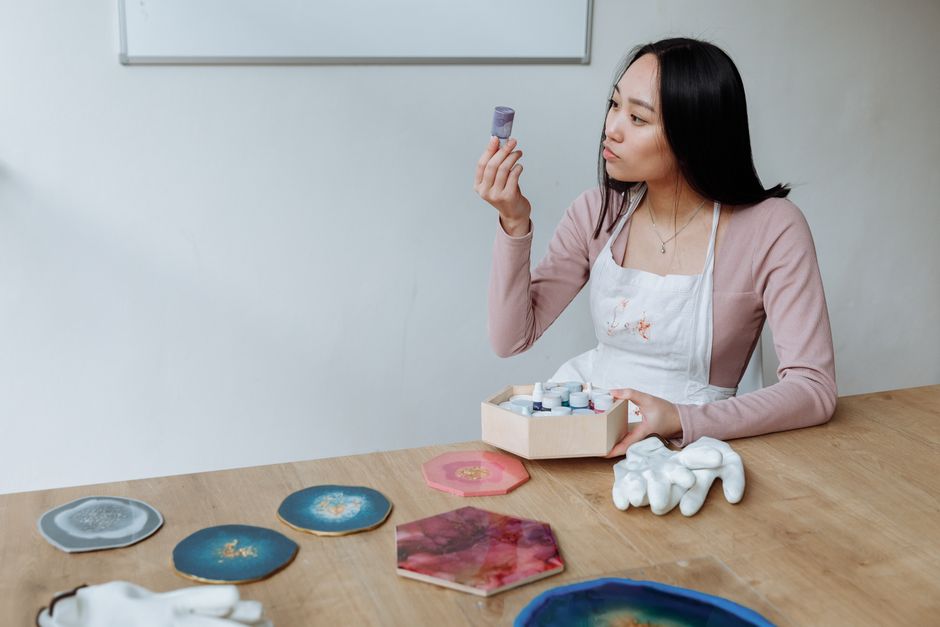 An adult woman examines pigment during a resin art project at a studio table.