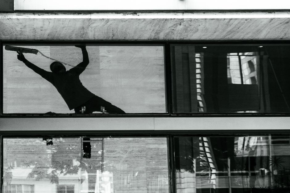 Silhouette of a window cleaner with squeegee on building glass, reflecting urban architecture.