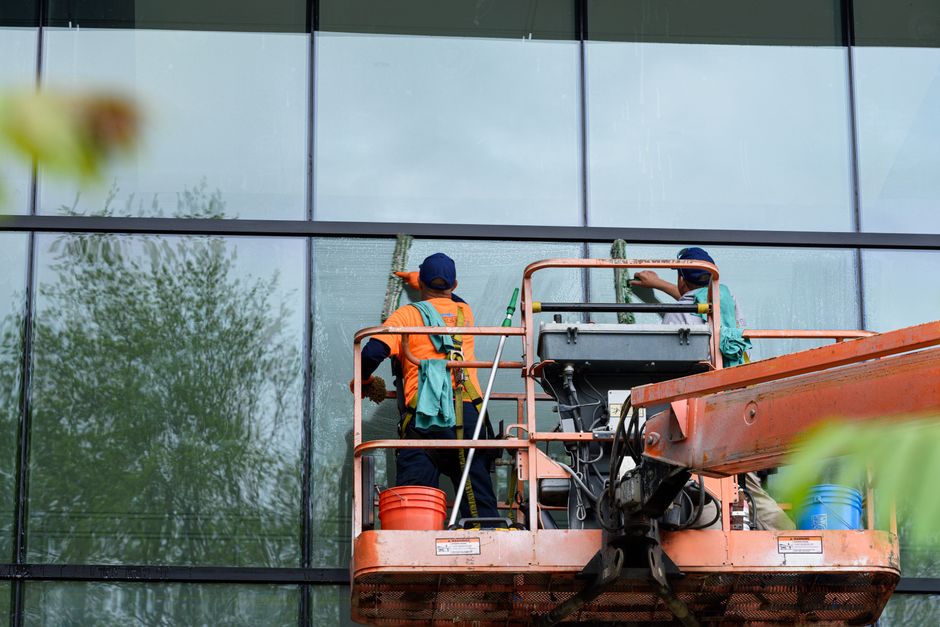 Two workers cleaning windows on a glass building facade using a lift platform, enhancing building aesthetics.