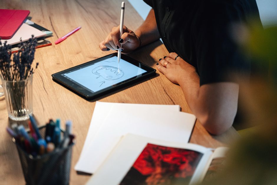 A person drawing on a digital tablet in a creative workspace, surrounded by art supplies.