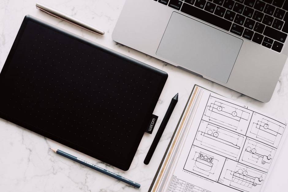 Top-down view of a desk setup including a laptop, drawing tablet, and design sketches.