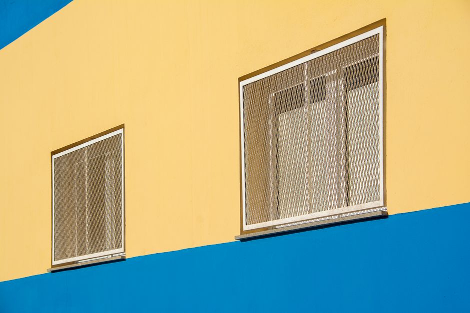 A vibrant yellow and blue building facade in Arinaga, Spain with wire mesh windows.