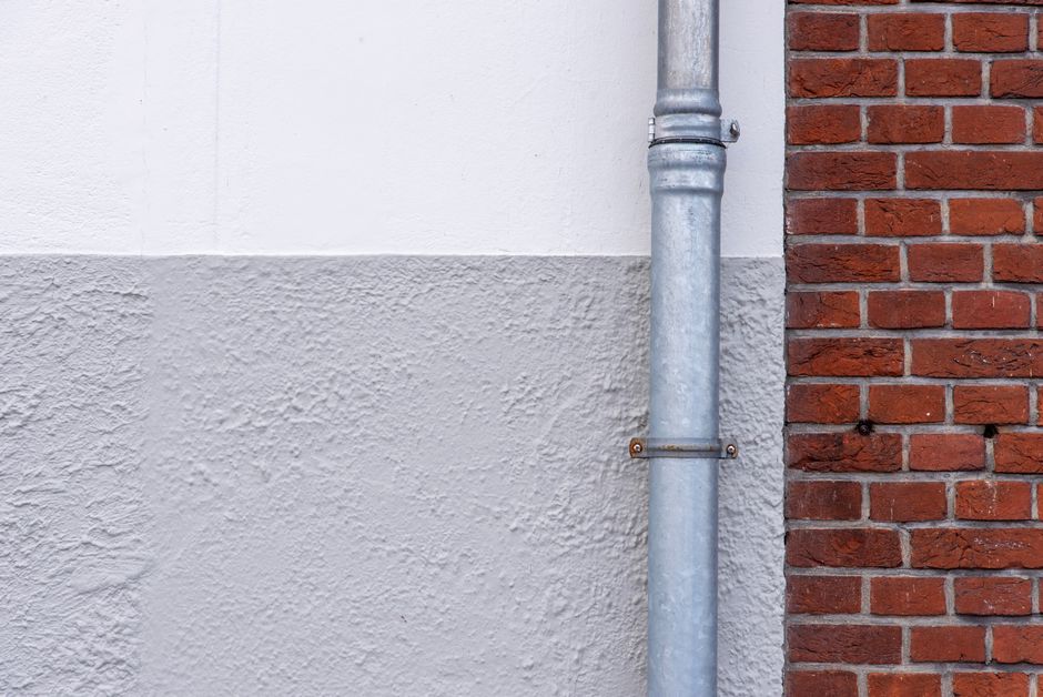 Close-up of a brick wall with a metal drainpipe against a textured white wall.