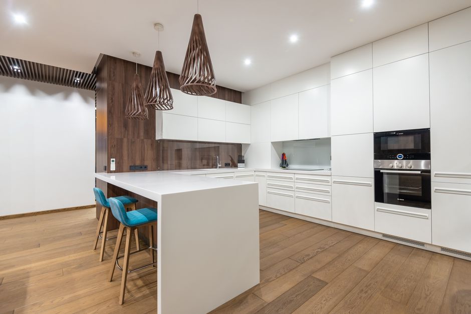 Chairs at table near white cupboards and modern kitchenware with oven in spacious stylish kitchen with hanging lamps in contemporary flat