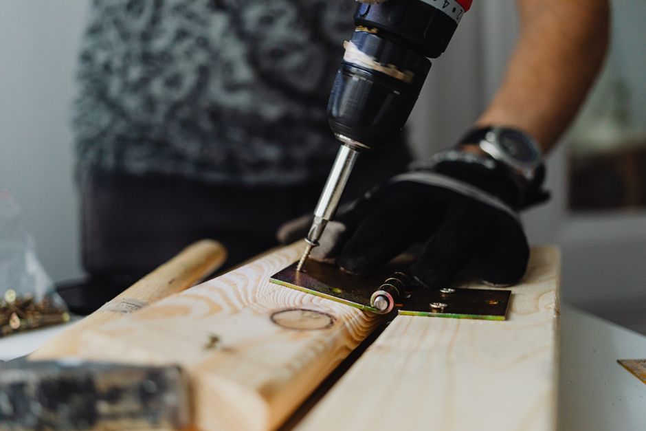 Focused close-up of a handyman using a drill on a wooden plank indoors.