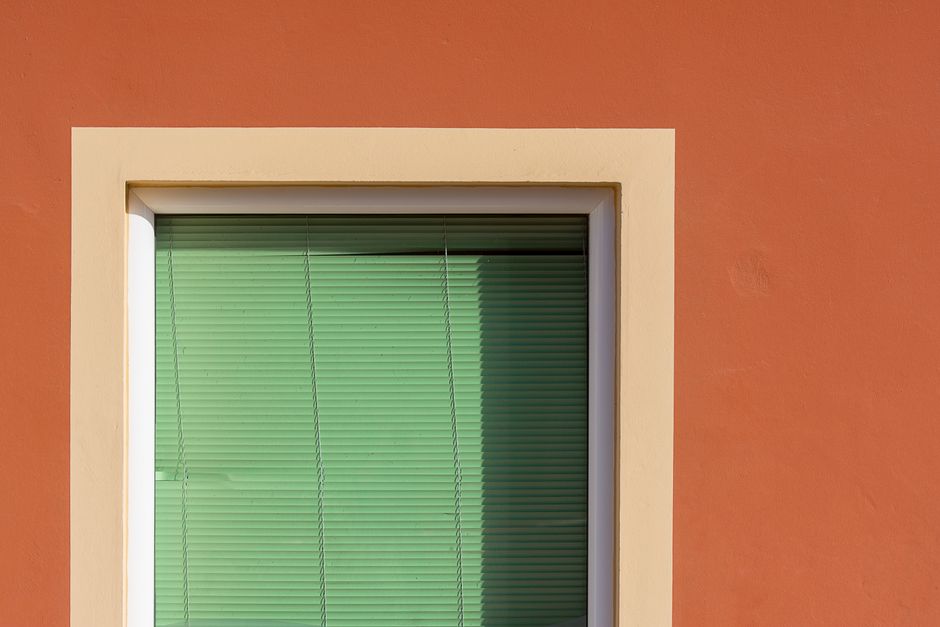 A minimalistic view of a green window with blinds set in an orange wall, creating a vibrant contrast.