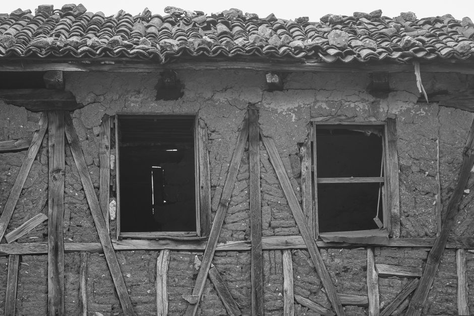 A black and white photo of an old, rundown house with wooden beams and two empty window frames.