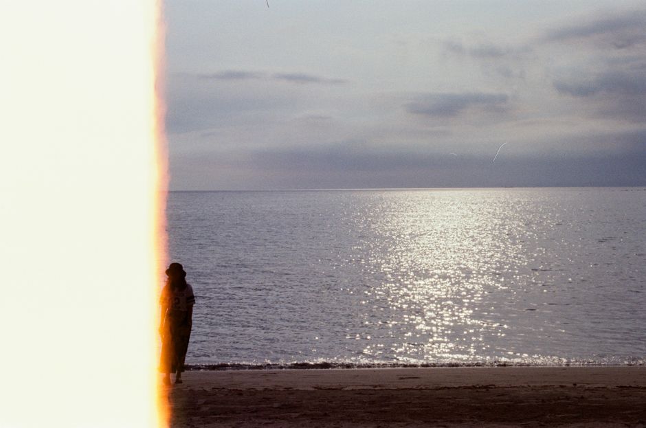 Artistic shot of a beach scene with a silhouette and unique film burn effect at sunset.
