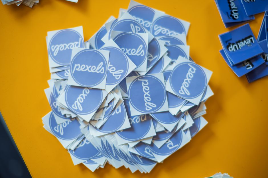 Pile of blue Pexels stickers on a vibrant yellow surface, top view.