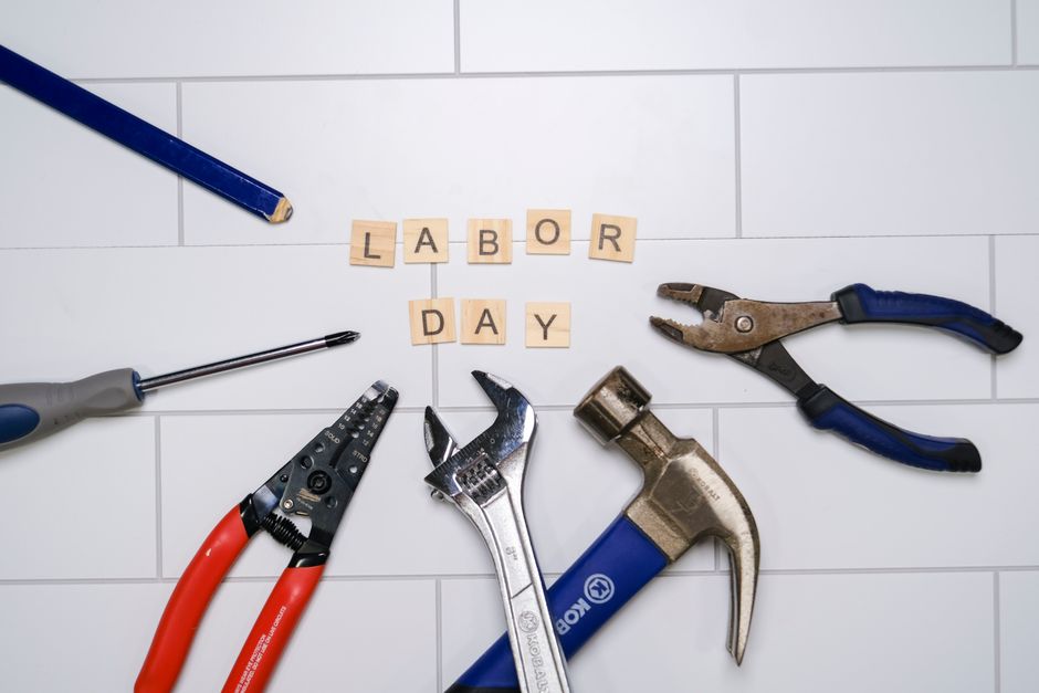 Flat lay of tools and 'Labor Day' tiles on a white surface, symbolizing labor celebration.