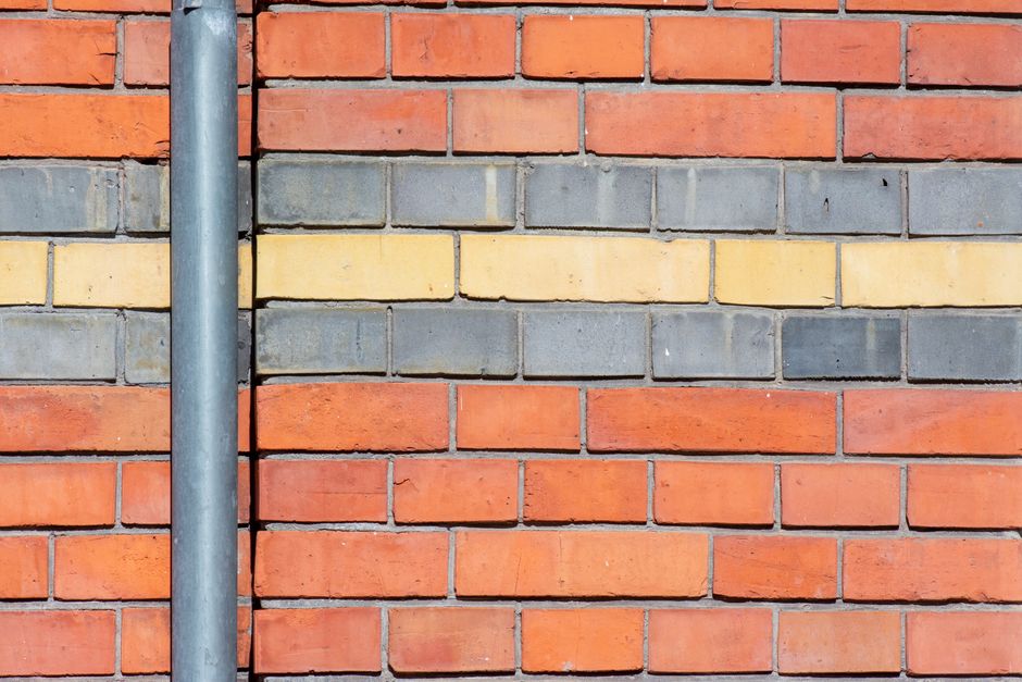 Vibrant brick wall featuring red, yellow, and gray bricks with a metal drainpipe.
