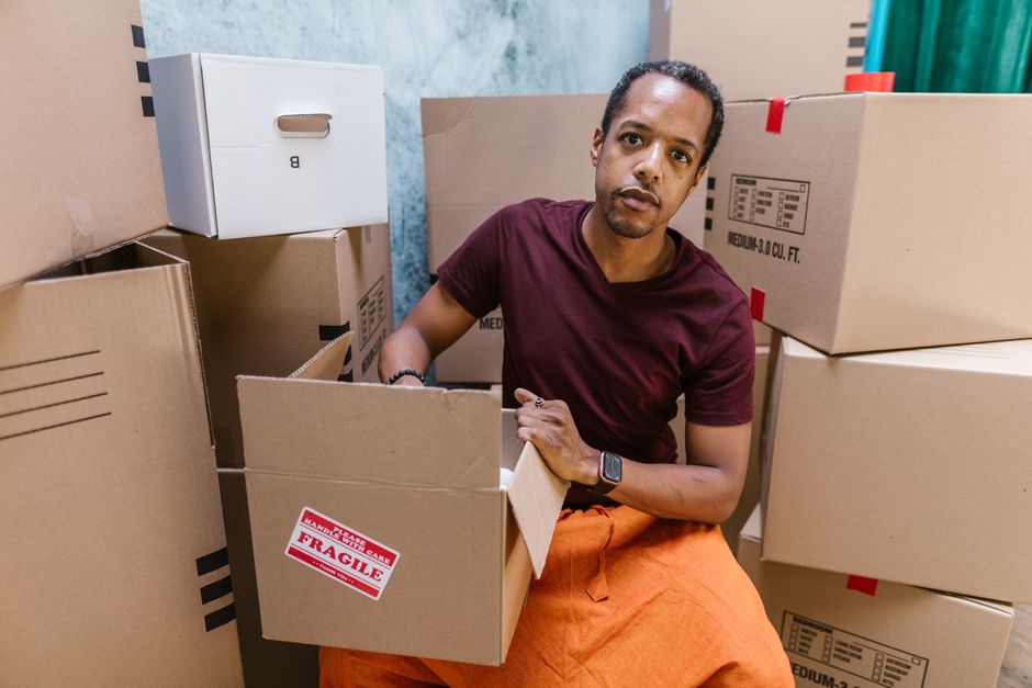 A man in a maroon shirt packing cardboard boxes for moving day, surrounded by labeled boxes.
