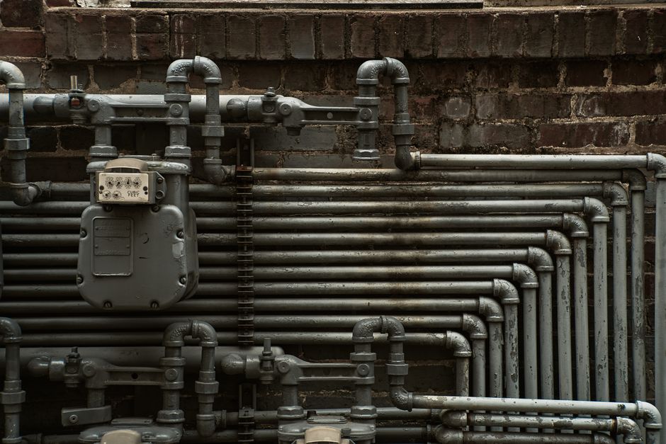 Detailed view of industrial steel pipes and a gas meter on a brick wall.