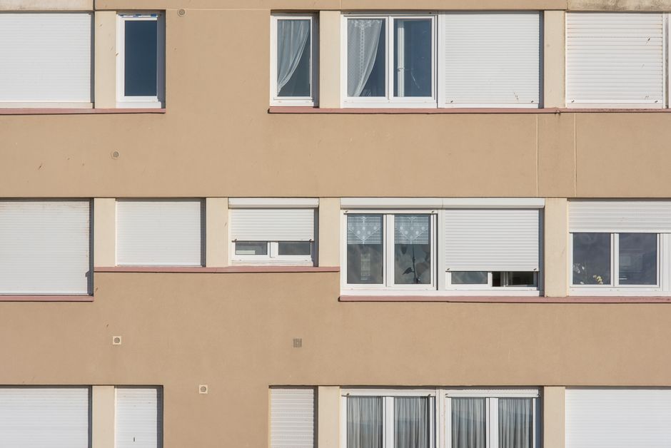Symmetrical arrangement of windows on a beige urban building facade with closed shutters.