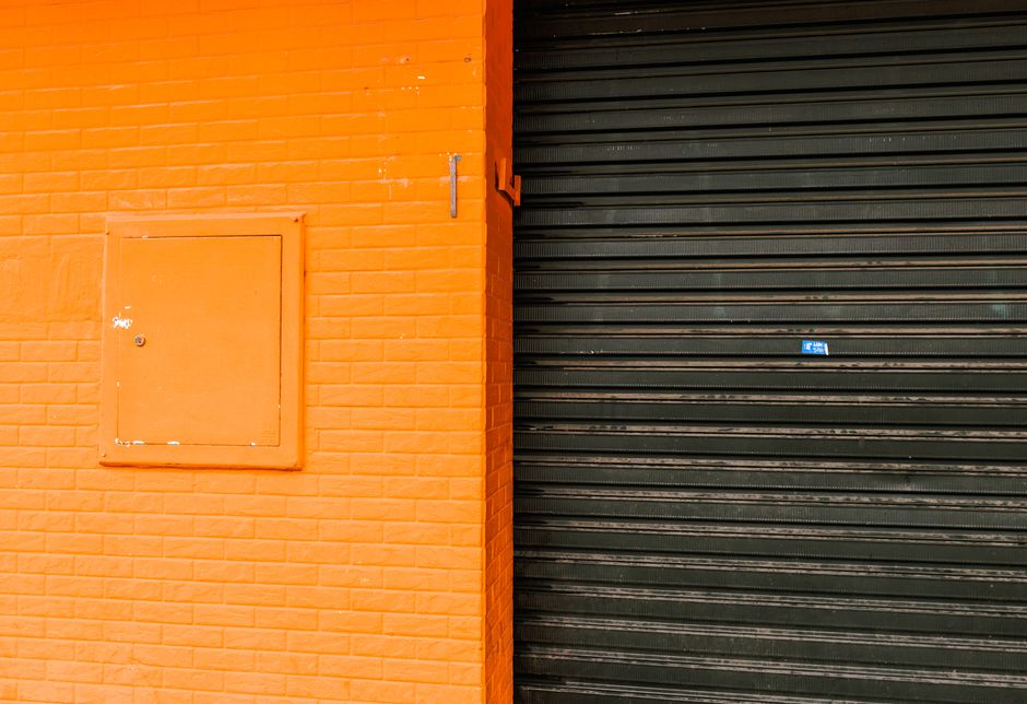 An orange-painted wall with imitation brick texture and a contrasting black roller door in an urban setting.