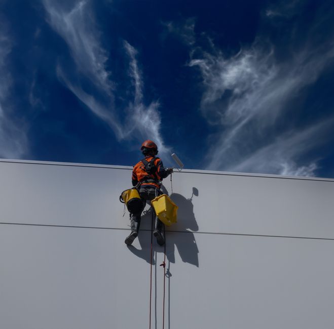 Back view of a worker painting a building wall outdoors in Auckland, New Zealand.