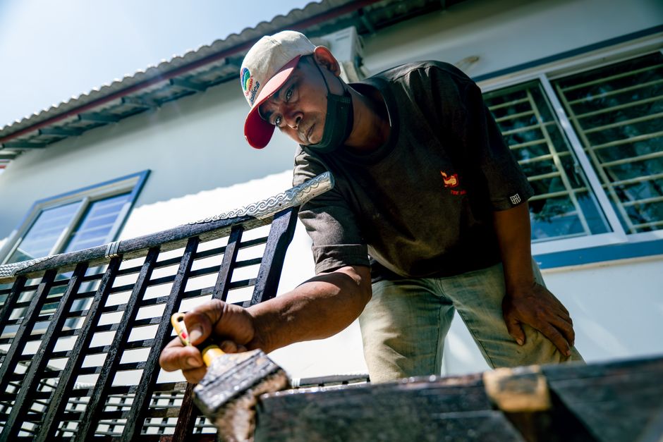 Man in cap painting a metal structure outdoors, showcasing skilled craftsmanship.