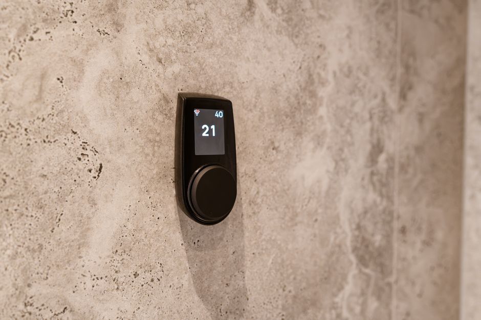 Close-up of a modern sauna temperature control device mounted on a textured stone wall, displaying a digital readout.