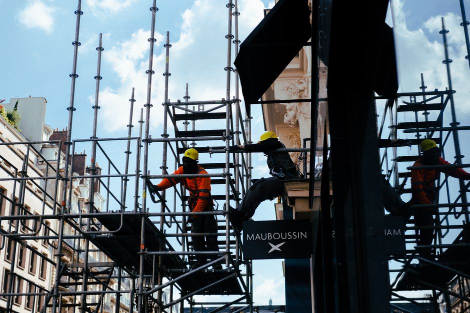 Silhouetted construction workers on scaffolding in an urban environment under blue skies.