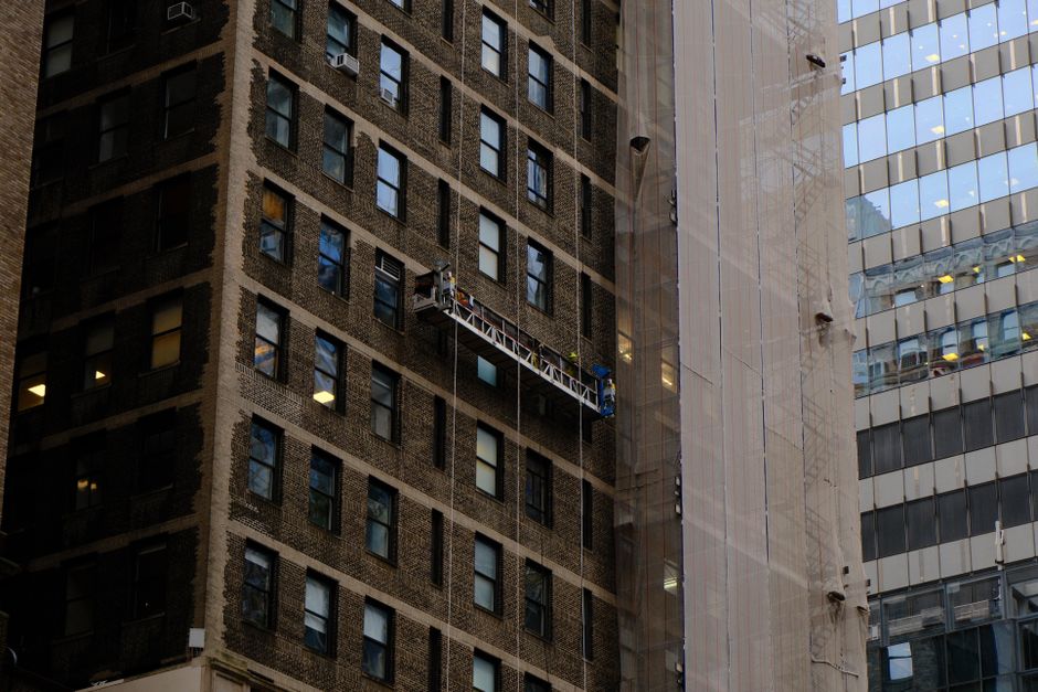 Workers on a suspended platform maintain a high-rise in New York City.