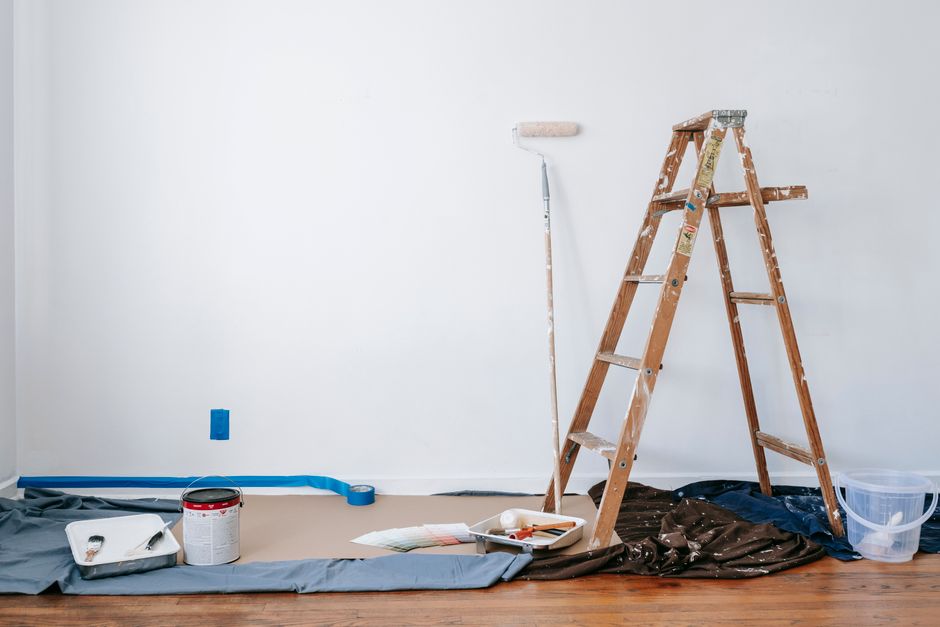 A room prepared for renovation with a ladder, paint supplies, and drop cloth.