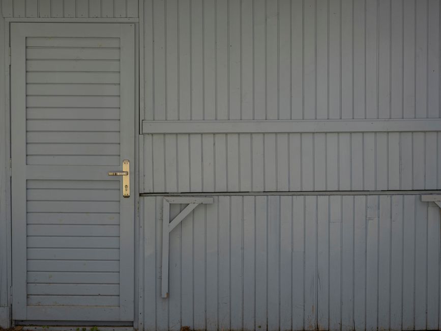 A simple and minimalistic view of a wooden building exterior featuring a closed door.