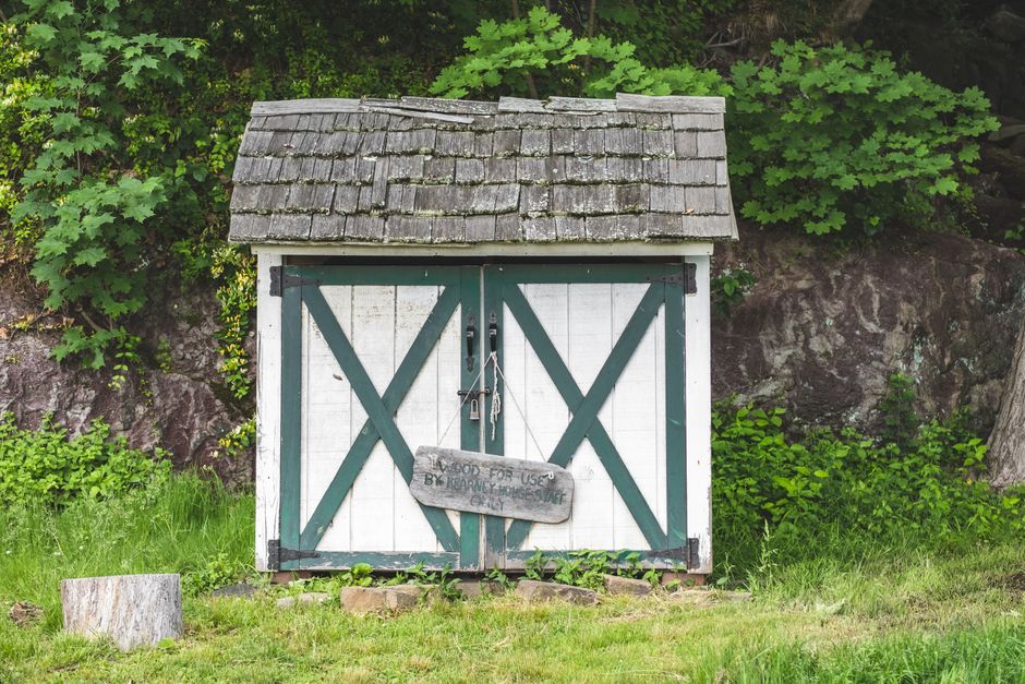 A small rustic wooden shed surrounded by lush green foliage in Alpine, NJ.