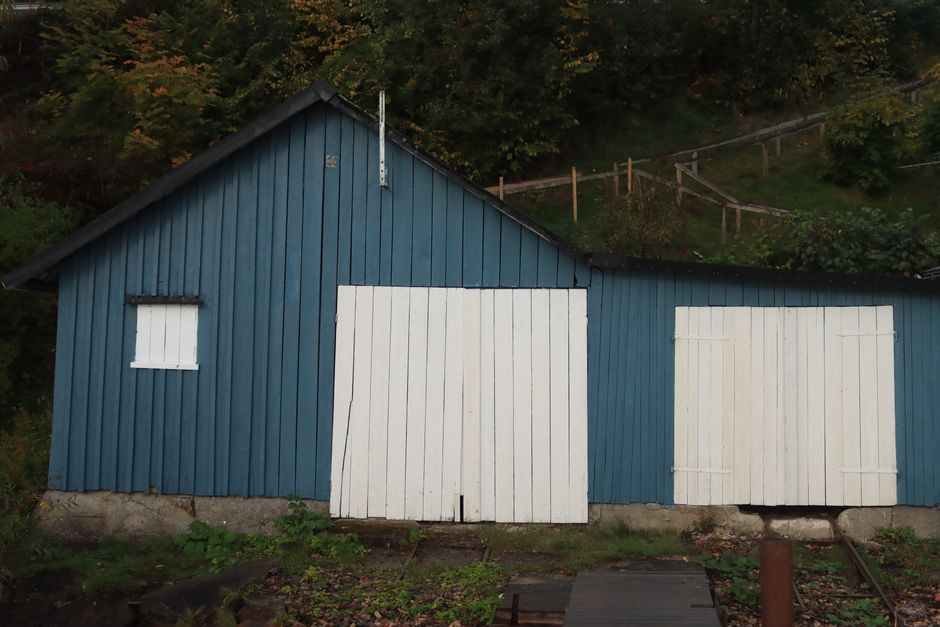 A charming rustic blue wooden cabin with distinctive white doors in a green setting.