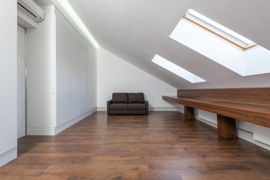 Spacious attic room featuring large skylights, a brown sofa, and wooden flooring.